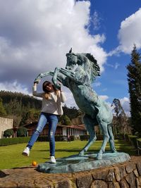 Low angle view of woman standing by horse statue in park