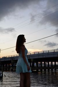 Woman standing by bridge against sky during sunset