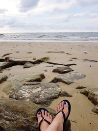 Low section of person on beach against sky