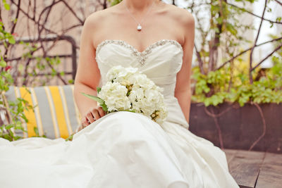 Midsection of bride sitting with white flowers bouquet