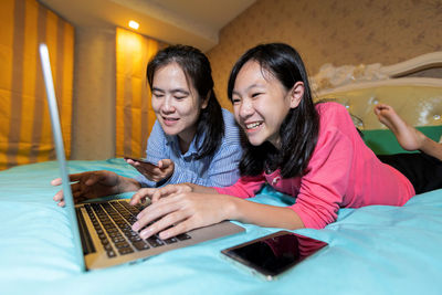 Smiling young woman using phone on bed at home