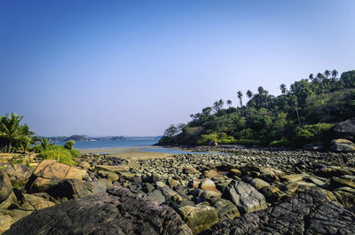 Rocks by sea against clear blue sky