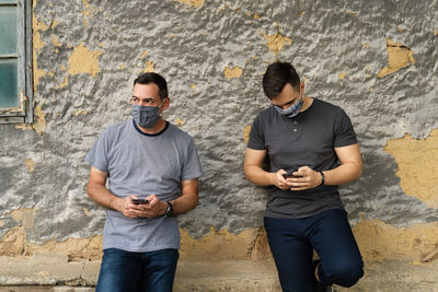 Full length of a young man using mobile phone against wall