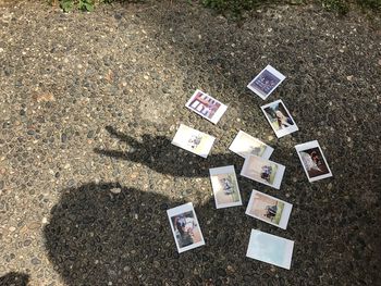 High angle view of shadow of person showing peace sign by photographs on road