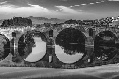 Arch bridge over river with reflection in city