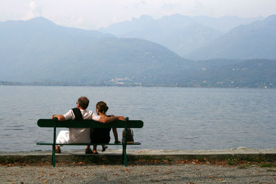 Rear view of men sitting on chair by lake