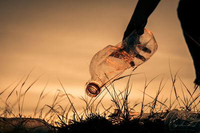 Cropped hand of person holding plastic bottle against sky