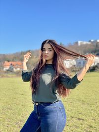 Young woman standing on field against blue sky