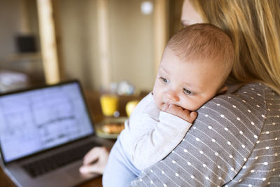 Mother with baby at home using laptop