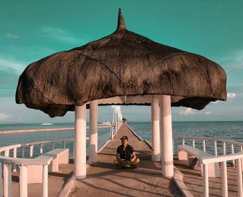 Man sitting below gazebo on pier against turquoise sky