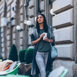 Young woman holding disposable cup while walking in city