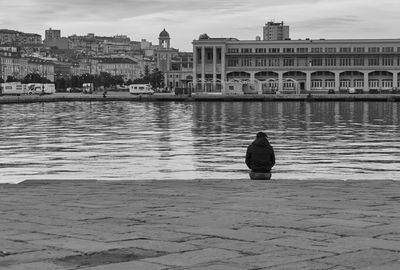 Rear view of man sitting on pier against buildings in city