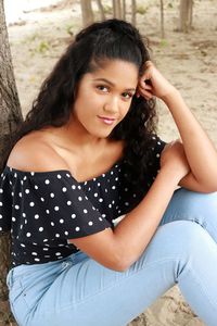 Portrait of young woman sitting by tree trunk at beach