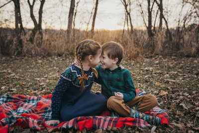 Boy and girl siblings smiling at each other sitting on red plaid blank