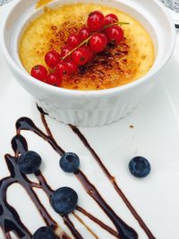 High angle view of fresh cherries served with creme brulee in bowl by blueberries on plate