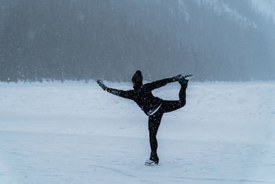 Female ice skater skating on frozen lake outside in snowstorm near forest in canada.