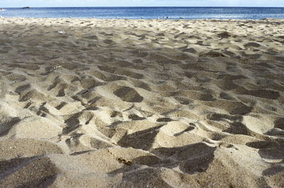 Footprints on sand at beach against clear sky