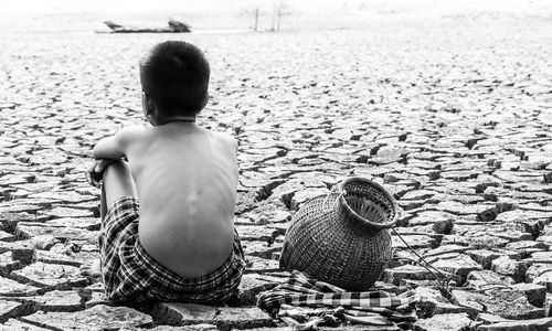 Rear view of shirtless boy sitting on drought field