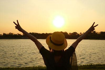 Rear view of person with arms raised against sky during sunset