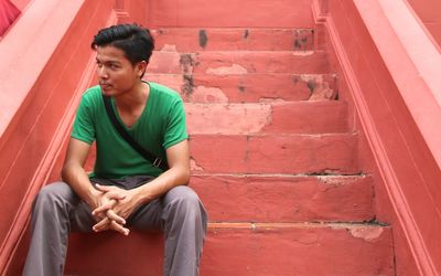 Young man looking away while sitting on steps