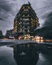 Illuminated buildings by street against sky at dusk