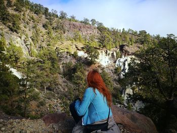 Rear view of woman sitting on rock against mountain