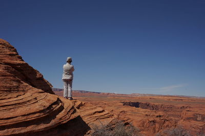 Rear view of man standing on rock against blue sky