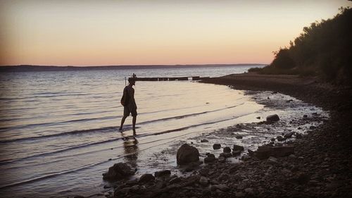 Man standing on beach against sky during sunset