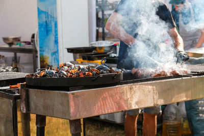 Man cooking bbq meat at festival outdoor. seafood paella. chef grilling sausages in park outside.