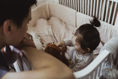 Father looking at baby son playing in crib at home