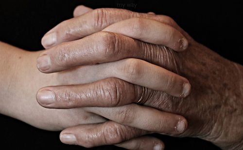 Cropped image of grandson holding hand of grandmother over black background