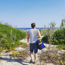 Rear view of young man walking towards beach against clear sky