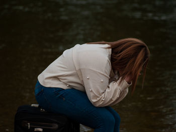 Woman sitting on luggage outdoors