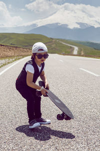 Child boy in a white cap sneakers and vest stands with a skate. road in mountains of mount everest