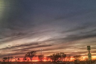 Illuminated trees against dramatic sky during sunset