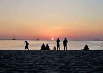 Silhouette people on beach against sky during sunset