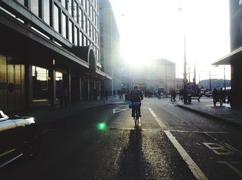 Rear view of person riding bicycle on city street by buildings against sky