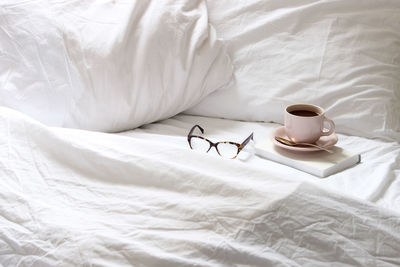 Elevated view of coffee cup and eyeglasses on bed