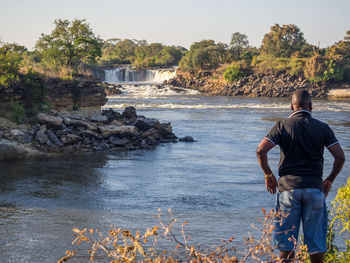 Rear view of man standing on riverbank at ngonye waterfall, zambia