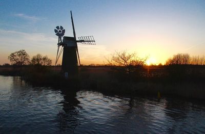 Silhouette statue by lake against sky during sunset