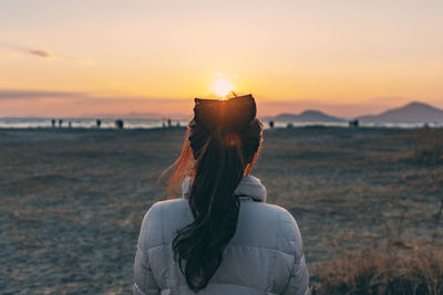 Rear view of woman standing at beach during sunset