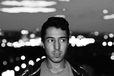 Serious young man looking away against defocused lights at night