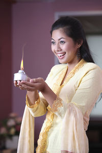 Young woman holding oil lamp while standing at home