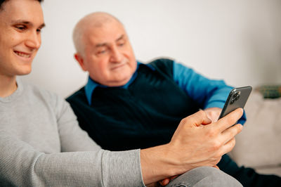 Grandfather with man using smart phone at home