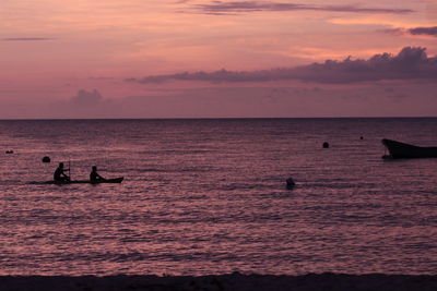 Silhouette people on sea against sky during sunset