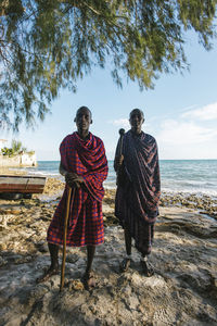 Two masai men in traditional clothes standing on the beach at sunset