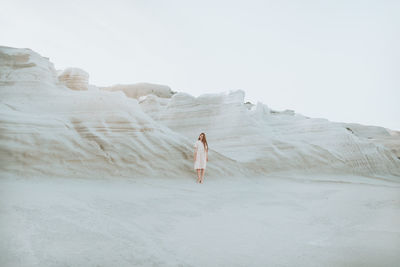 Rear view of woman standing on rock against sky