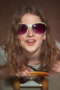 Portrait of happy girl wearing sunglasses while lying on skateboard at home