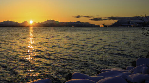 Low section of person on sea against sky during sunset