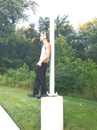 Side view of young man standing against trees